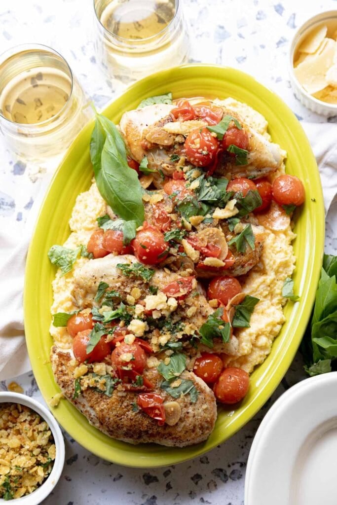 Seared chicken breasts with cherry tomato sauce and polenta on a serving platter.