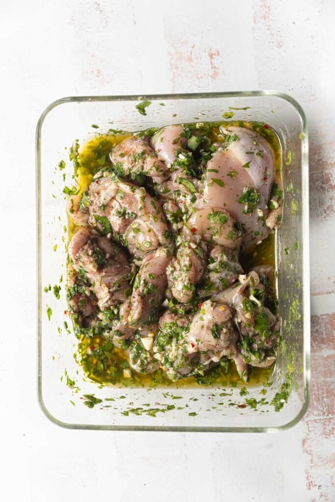 Marinating chicken thighs in chimichurri sauce.