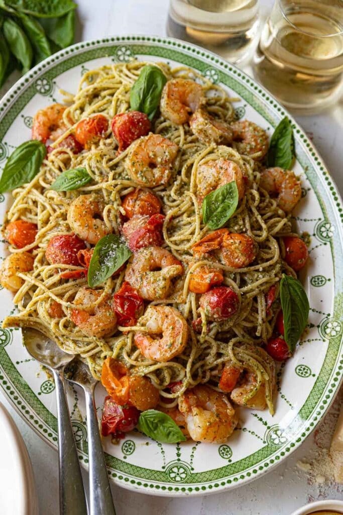Shrimp spaghetti with pesto and cherry tomatoes on a serving platter.