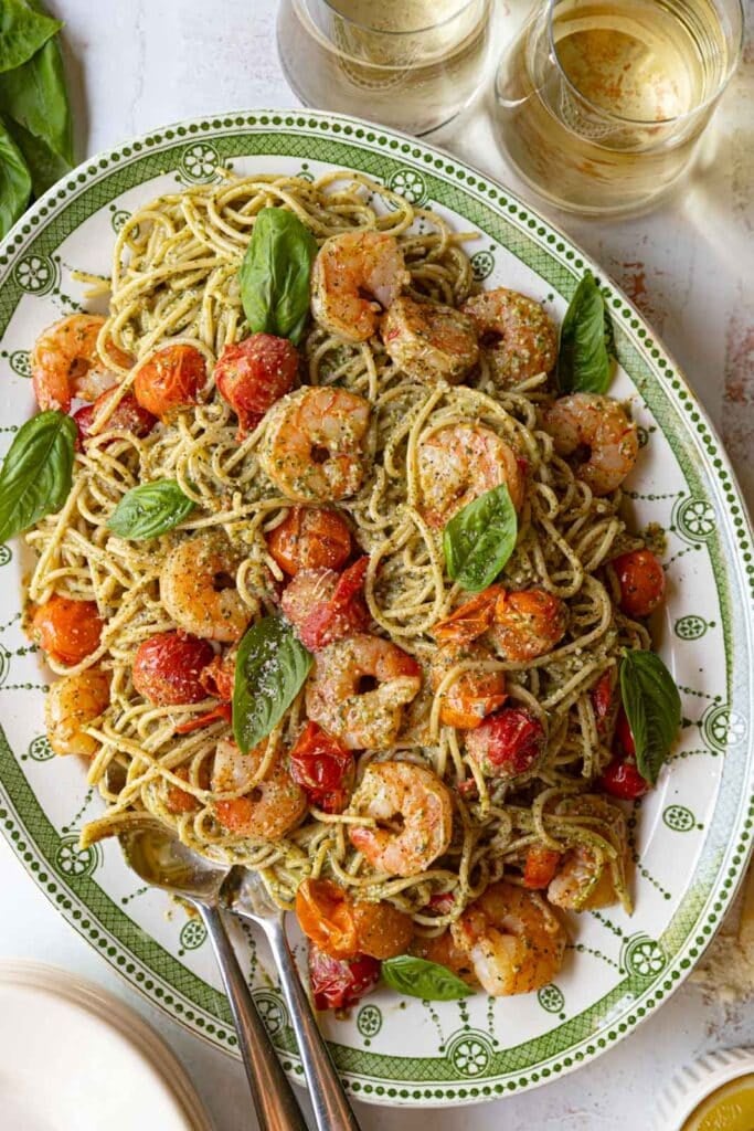 Shrimp spaghetti with pesto and cherry tomatoes on a serving platter.