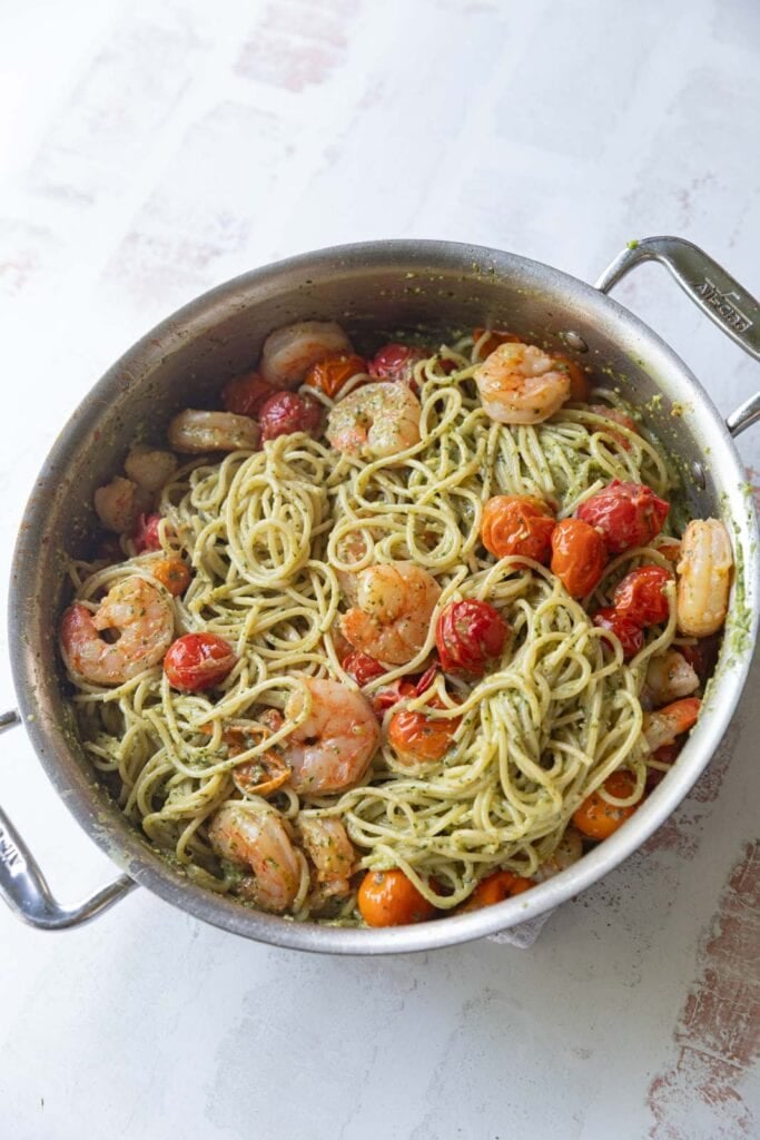 Pesto spaghetti with shrimp and tomatoes in a pan.