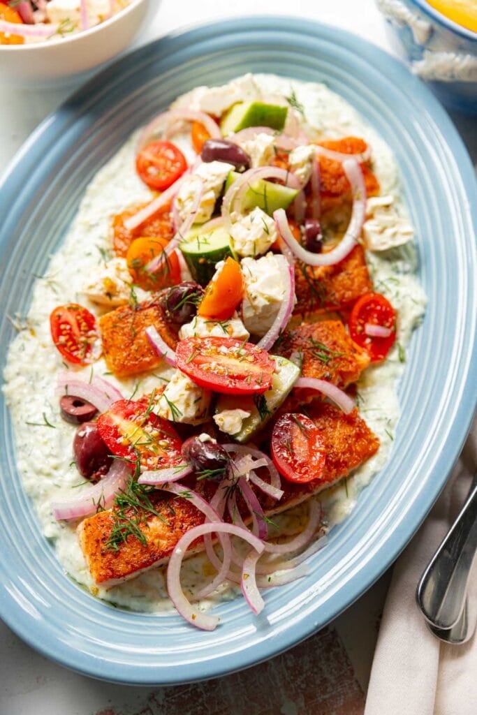 Salmon with yogurt sauce and greek salad on a blue platter.