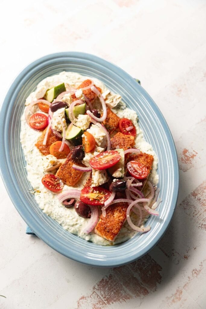 Salmon with yogurt sauce and greek salad on a blue platter.