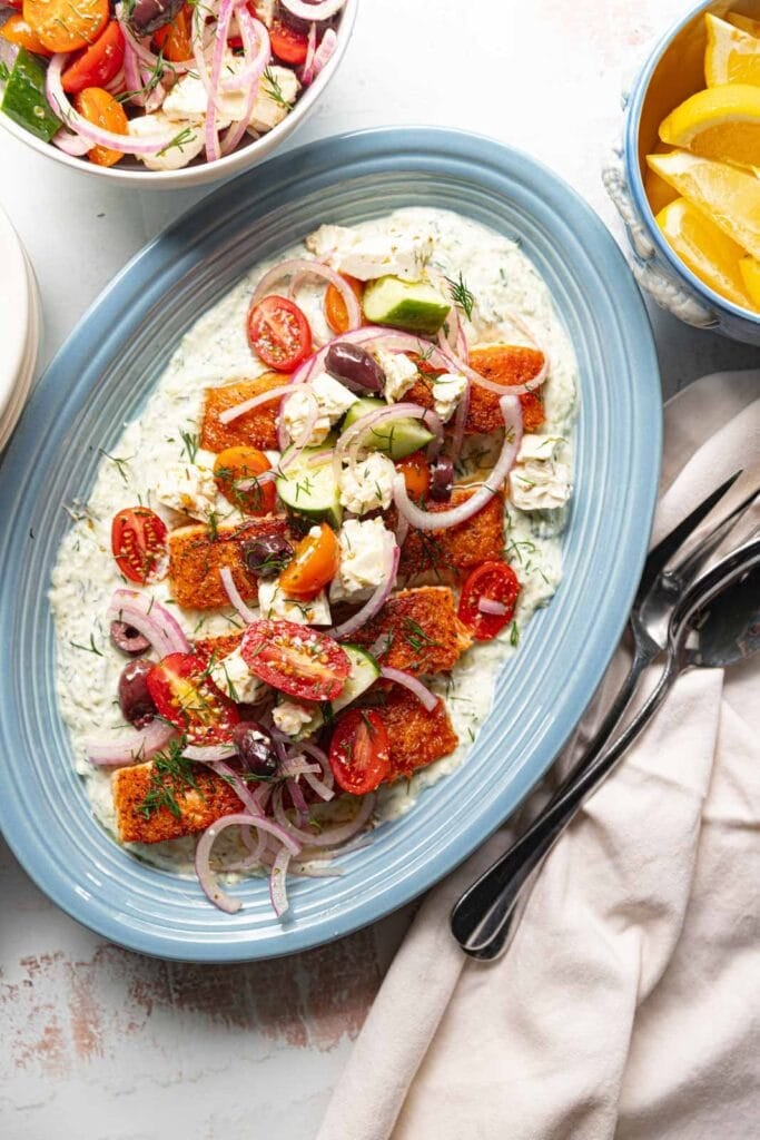 Salmon with yogurt sauce and greek salad on a blue platter.
