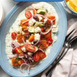 Yogurt sauce, salmon, and greek salad on a blue serving platter.